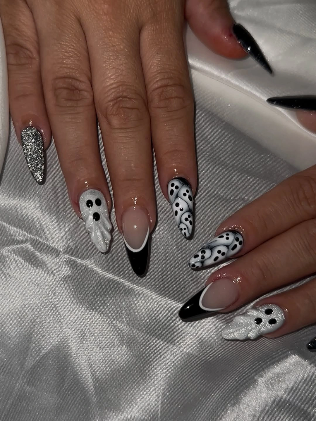 White Halloween nails with black ghost faces, dots, and dark pointed edge details