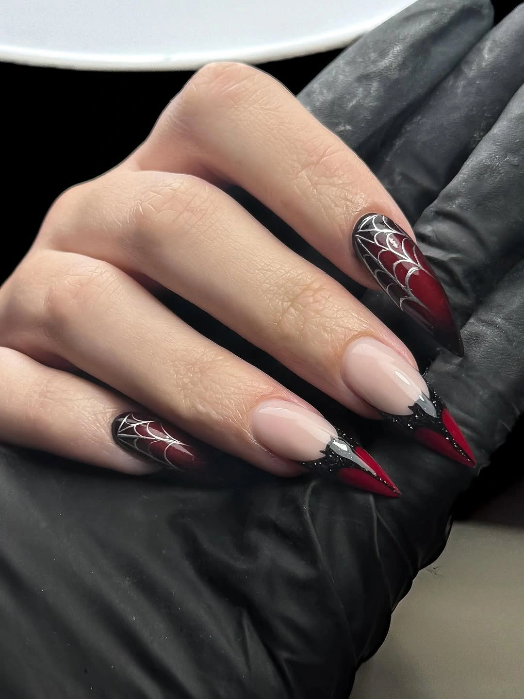 Long black and red Halloween nails with spiderweb graphics and sharp red tips