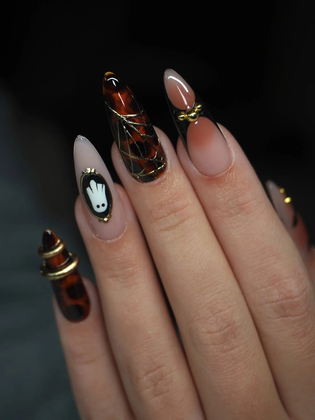 Nude and black Halloween nails with pumpkin and ghost motifs plus one amber patterned accent