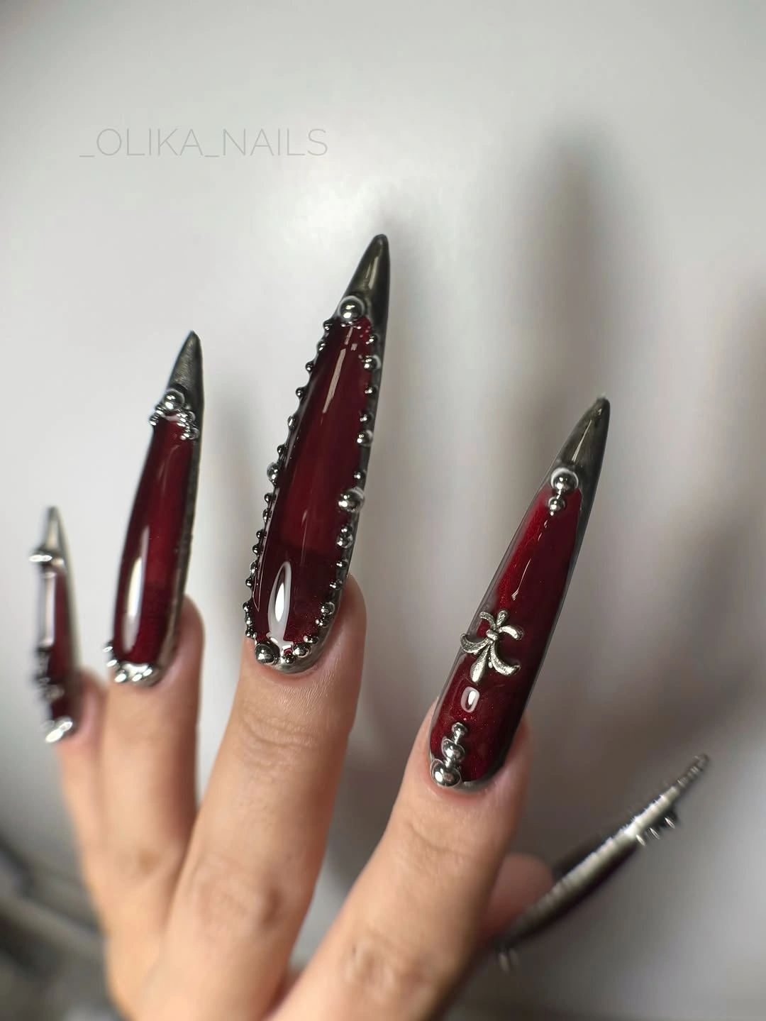 Very long burgundy stiletto Halloween nails with silver and black metallic stud details