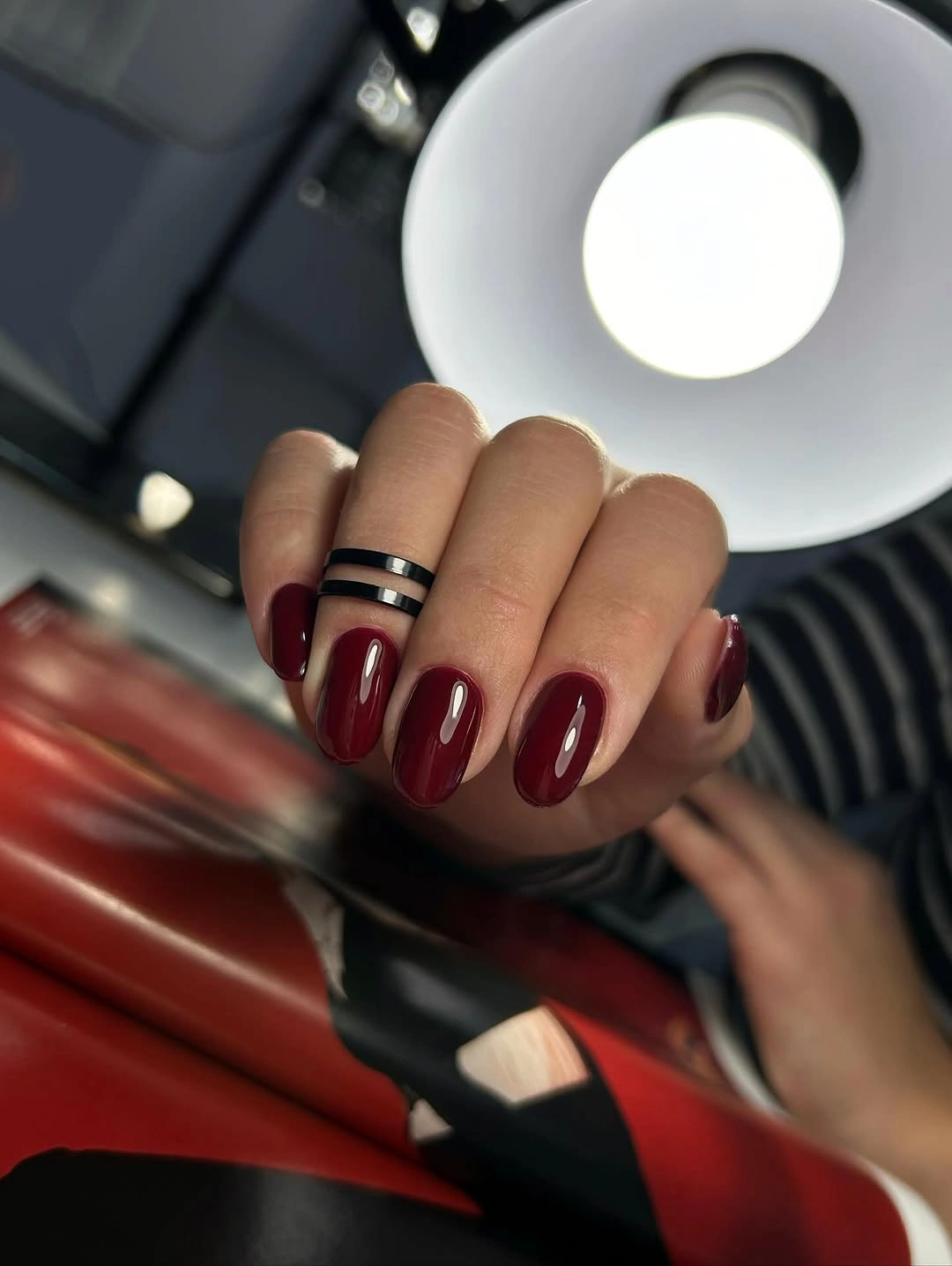 Glossy dark maroon almond nails in low light