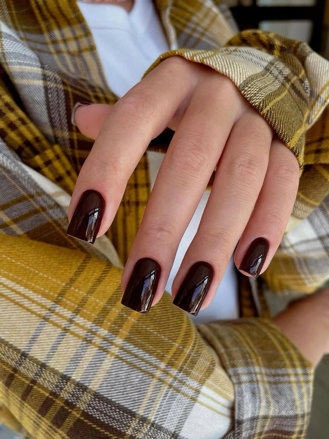 Near black burgundy soft square nails beside warm plaid