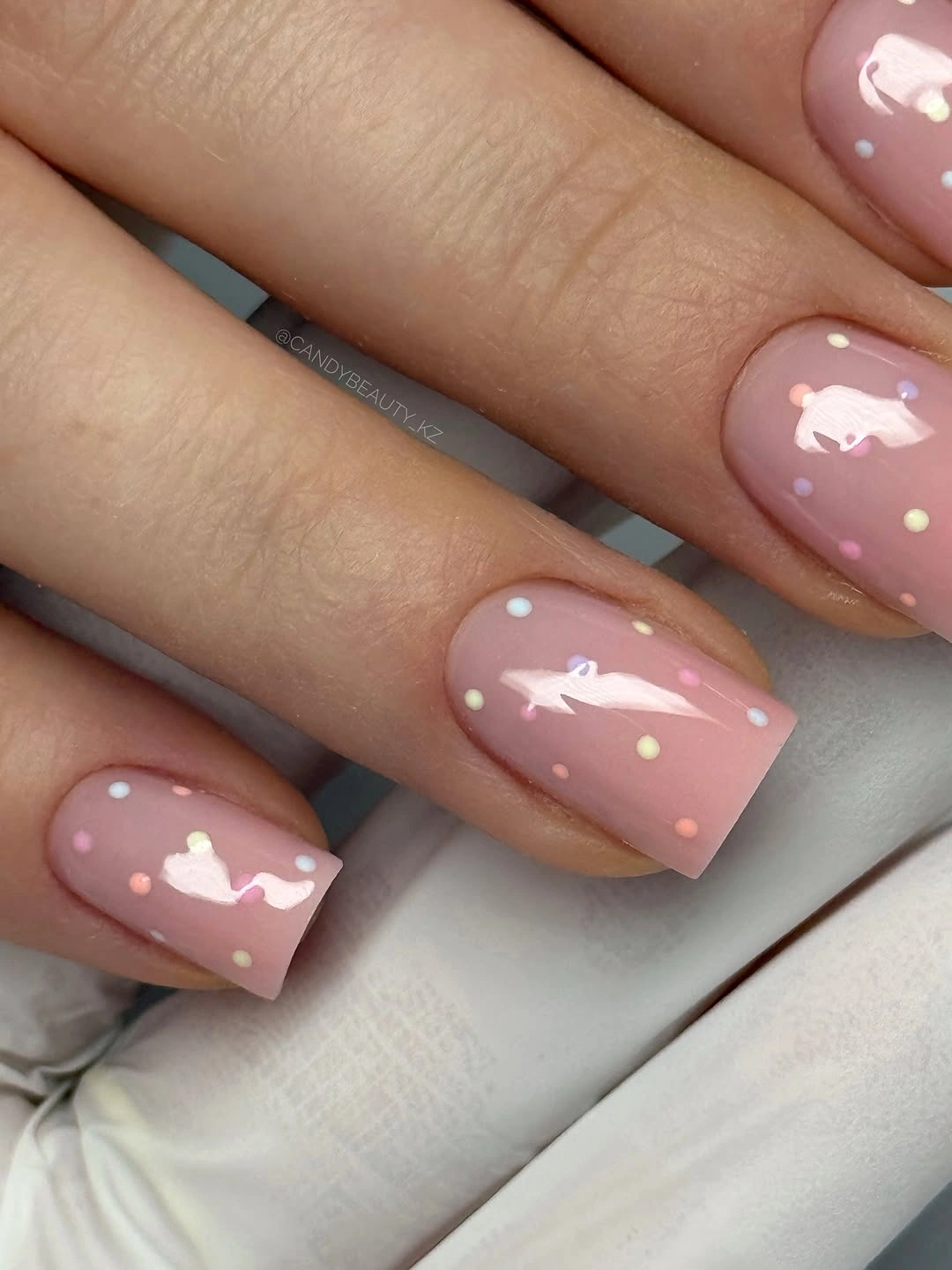 Short pale pink square nails with tiny white dots and bow details