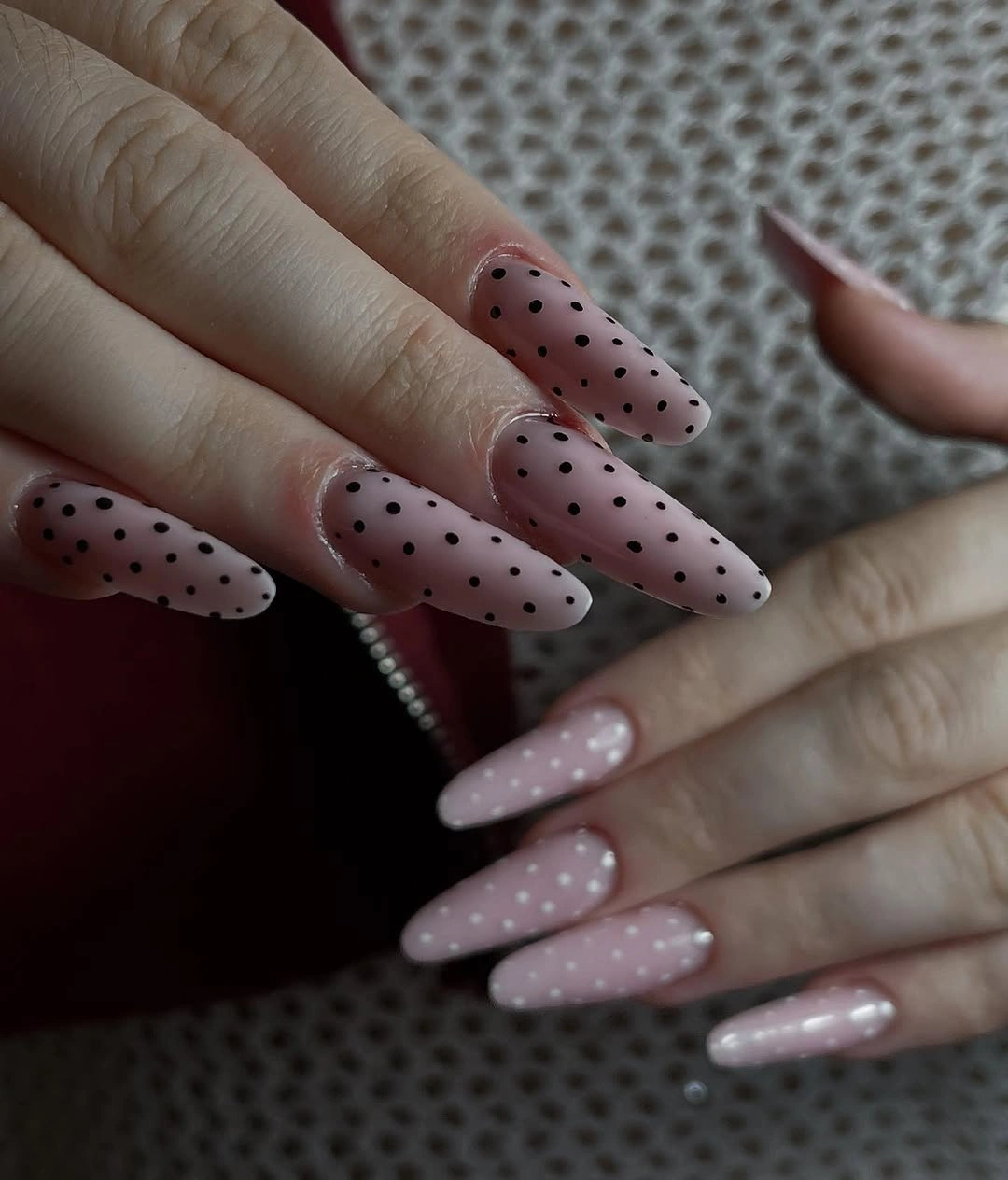 Long pale pink pointed nails with small evenly scattered black dots