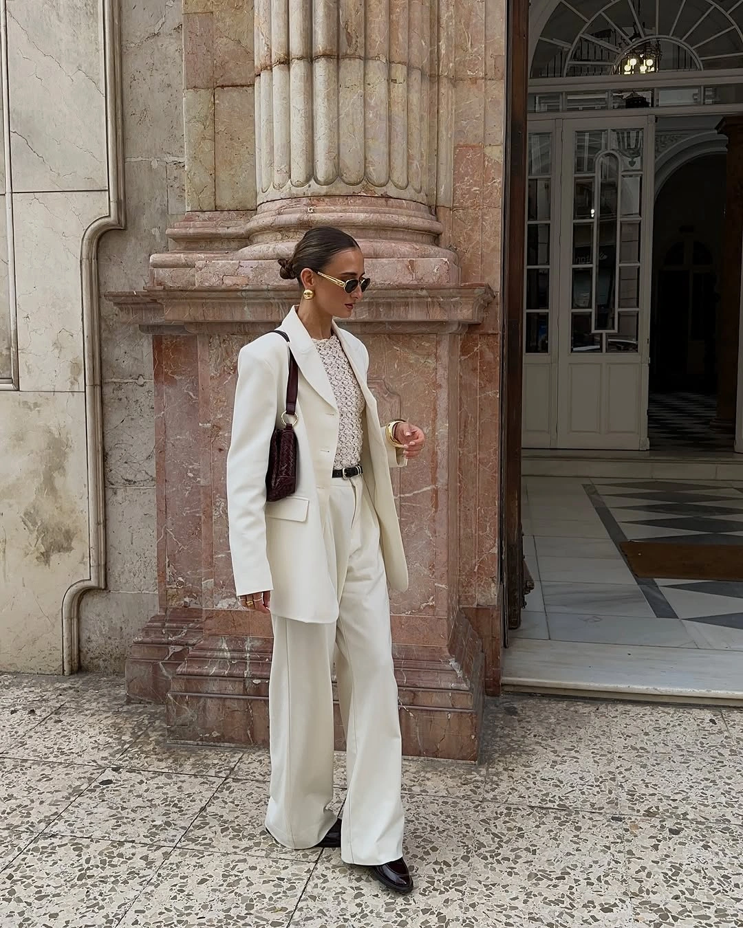 Cream suit with dark accessories and sunglasses at a doorway