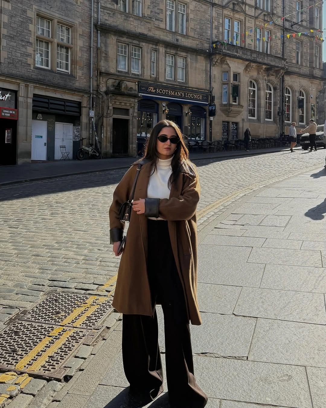 Long brown coat with white high neck and black wide trousers