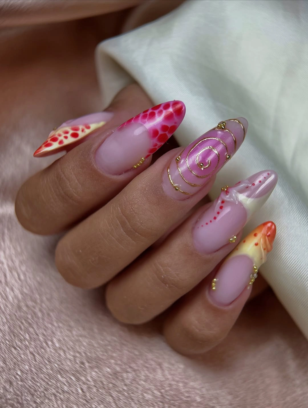 Long almond nails with sheer pink base and gold-toned red accents