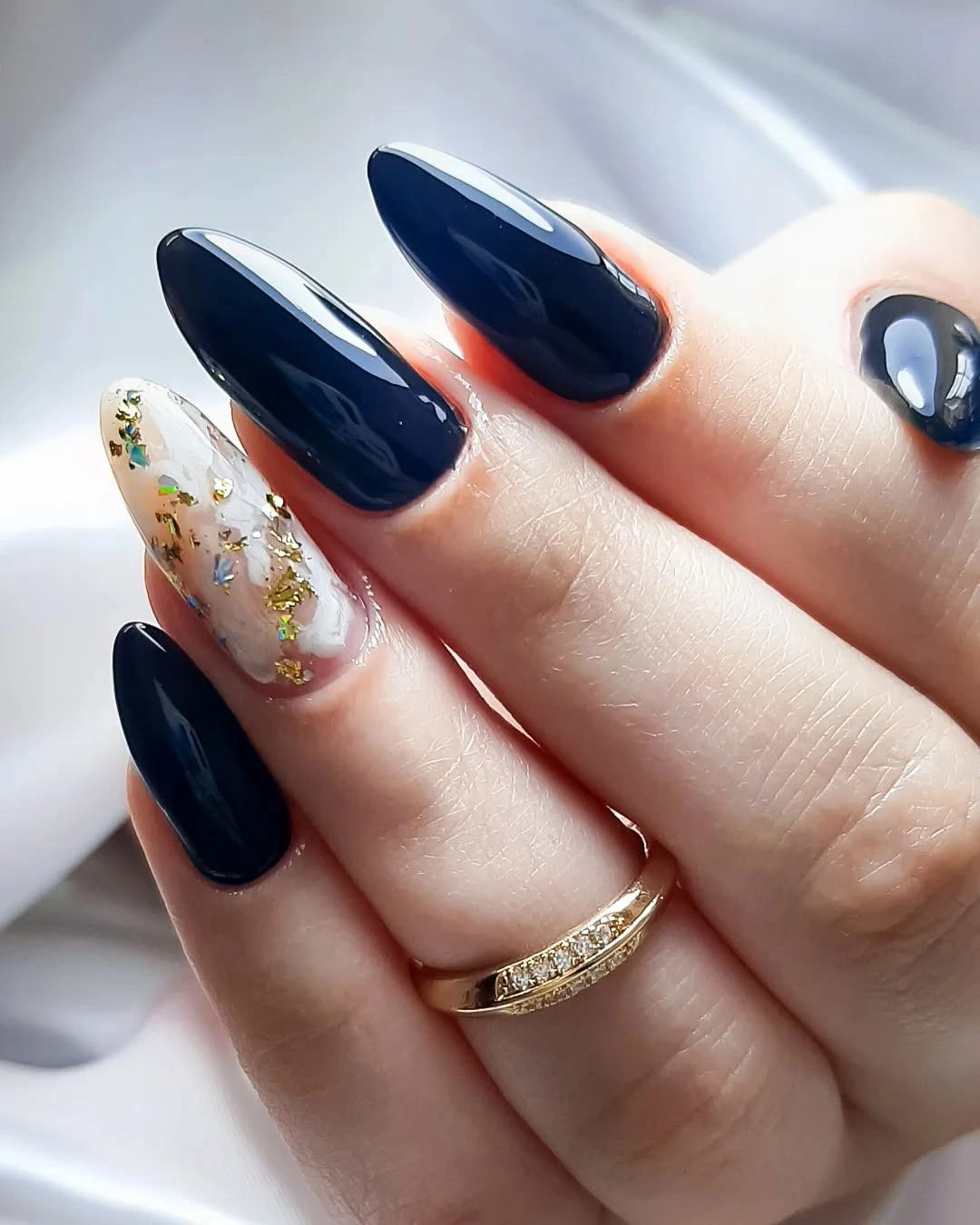 Glossy navy almond nails with translucent accent and fleck-like pieces