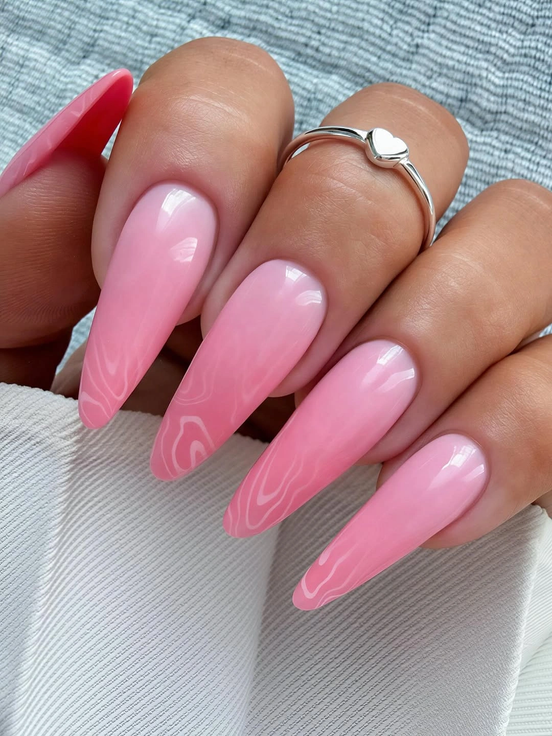Long glossy pink almond nails with pale swirl lines near tips