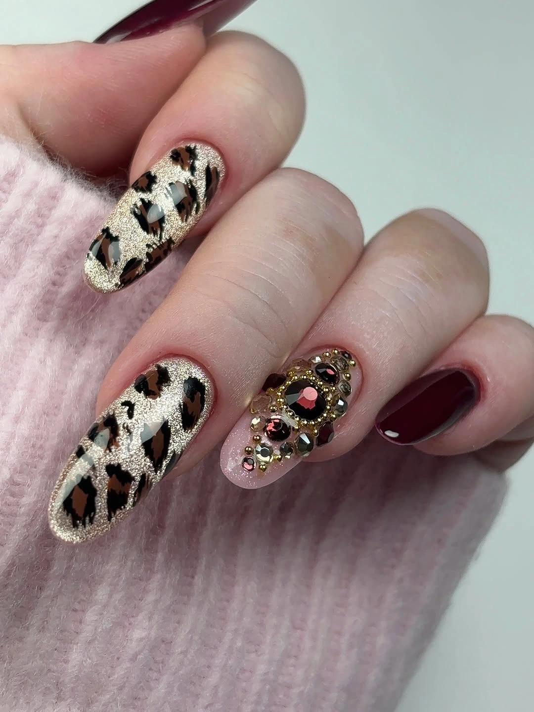 Medium-long almond nails with burgundy polish, gold leopard pattern and raised-looking accent