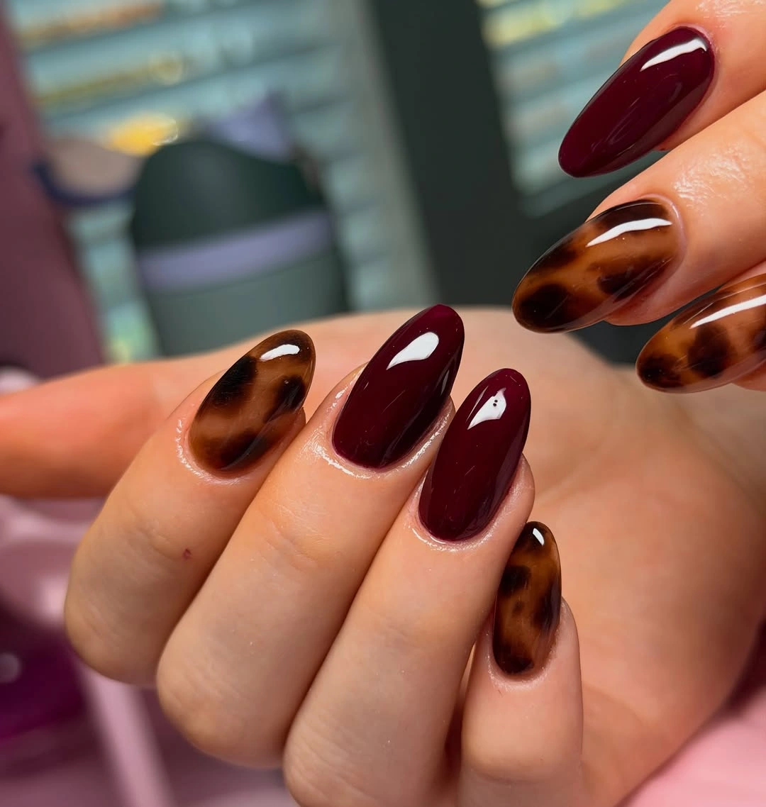 Medium-long almond nails with burgundy polish and tortoiseshell-like pattern