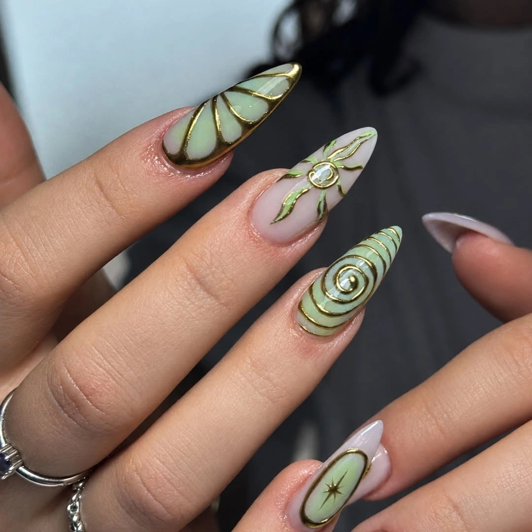 Long pointed almond nails with green panels and gold-toned botanical lines