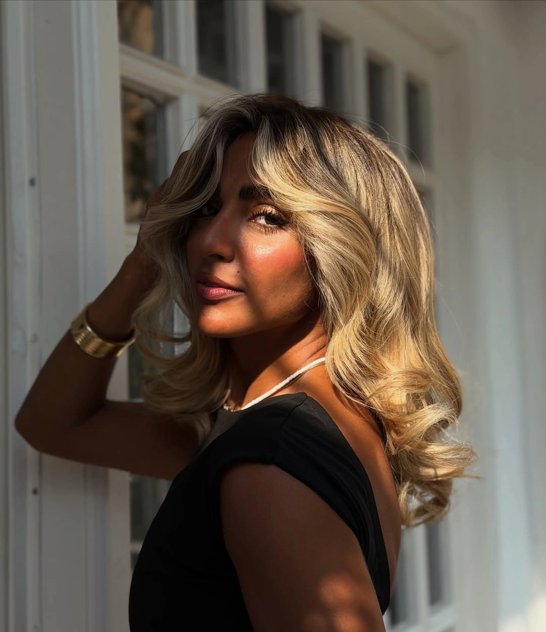 Medium-length warm blonde curls with deeper roots and golden brightness