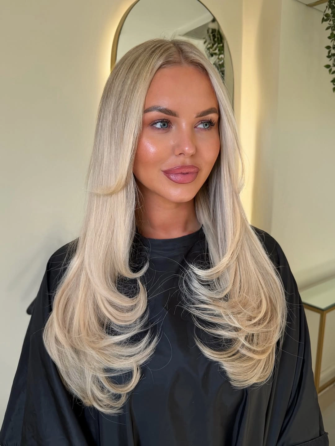 Long layered blonde hair with cool beige roots and curved ends