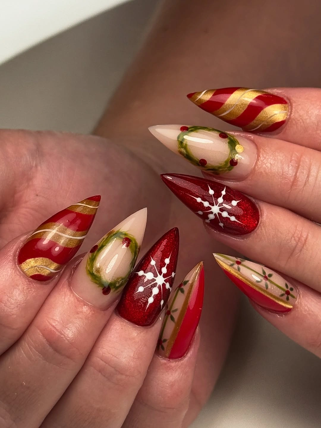 Long almond nails with red, nude, gold, green, and snowflake details