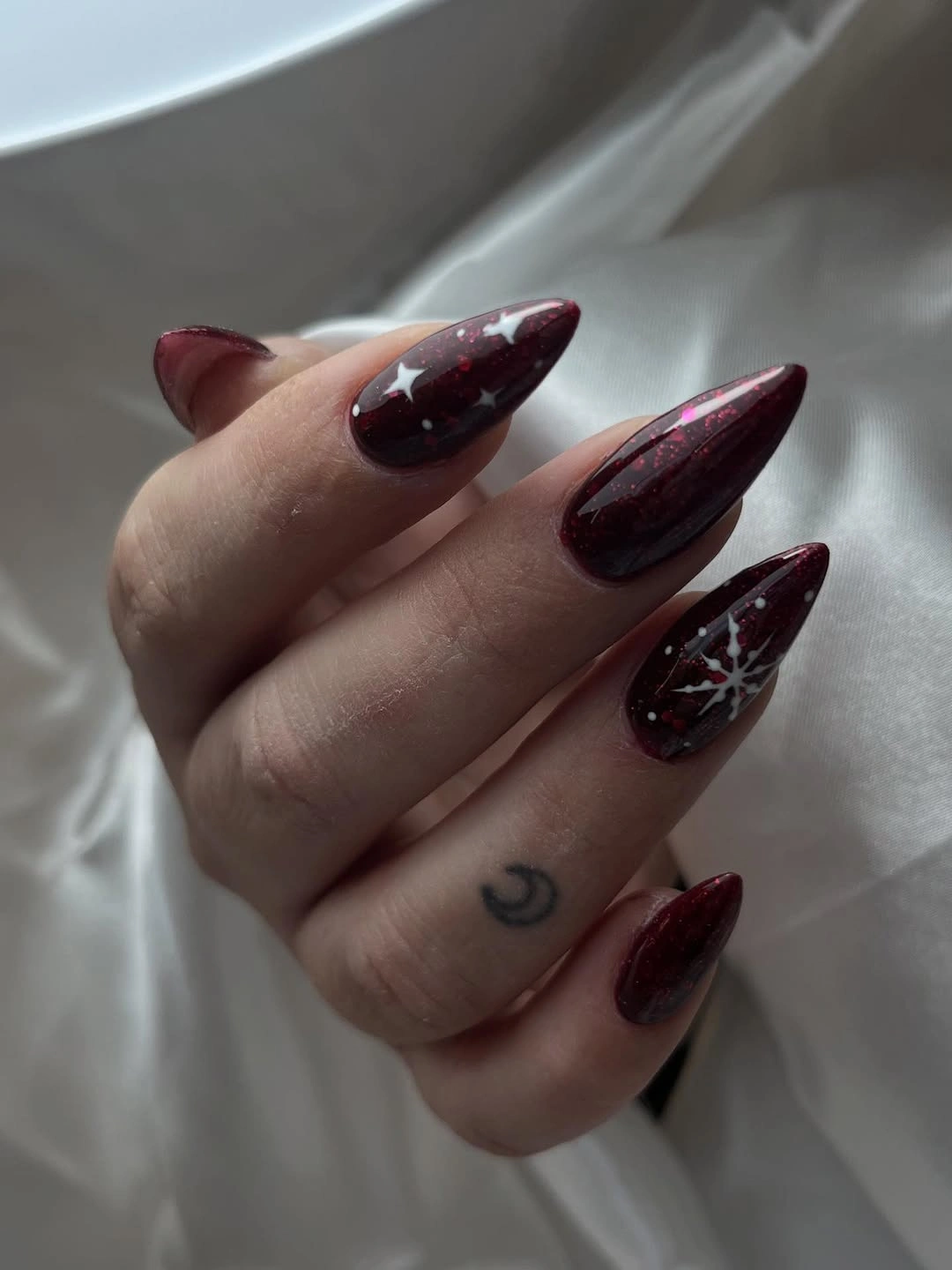 Pointed burgundy almond nails with white stars dots and snowflake