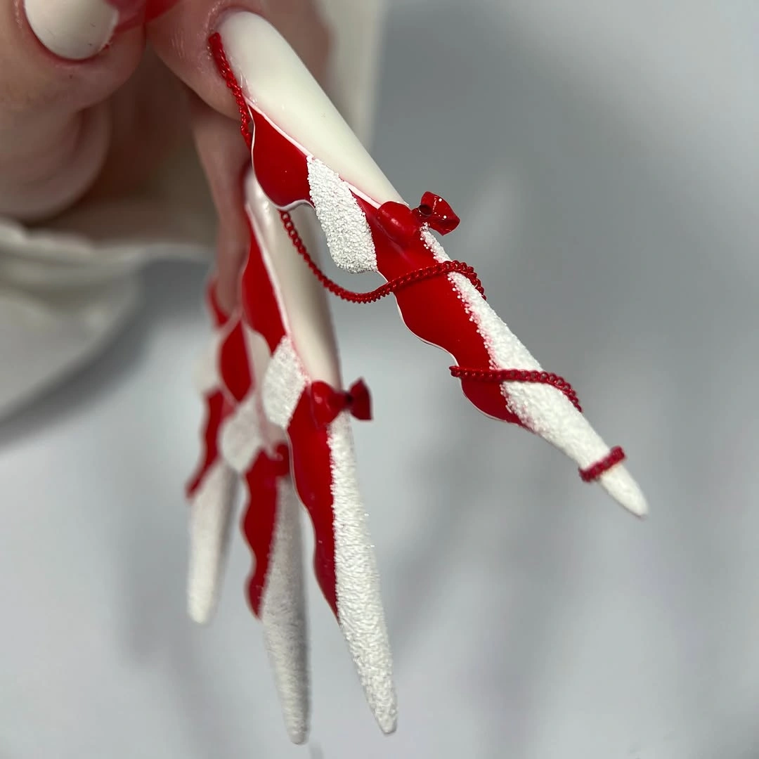 Long stiletto nails with red sections, white bands, and bows