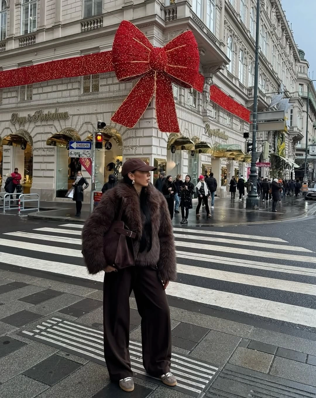 Dark brown shaggy jacket, black trousers, cap, and handbag beneath red holiday bow