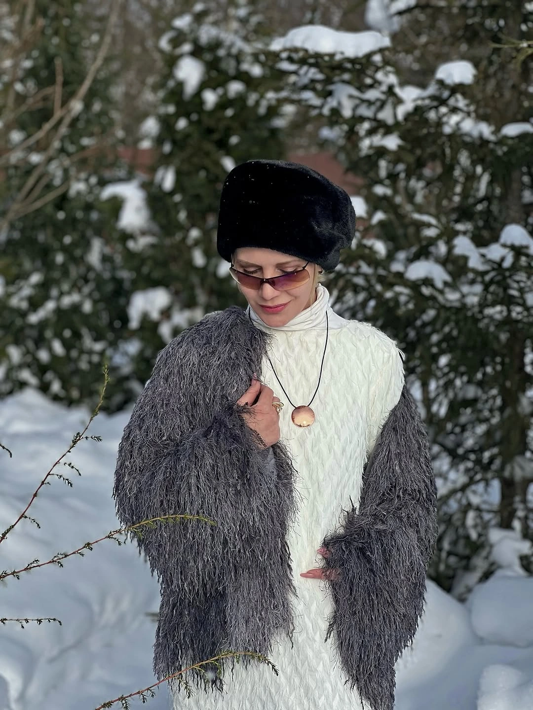 White textured high-neck dress, gray shaggy layer, black hat, glasses, and pendant