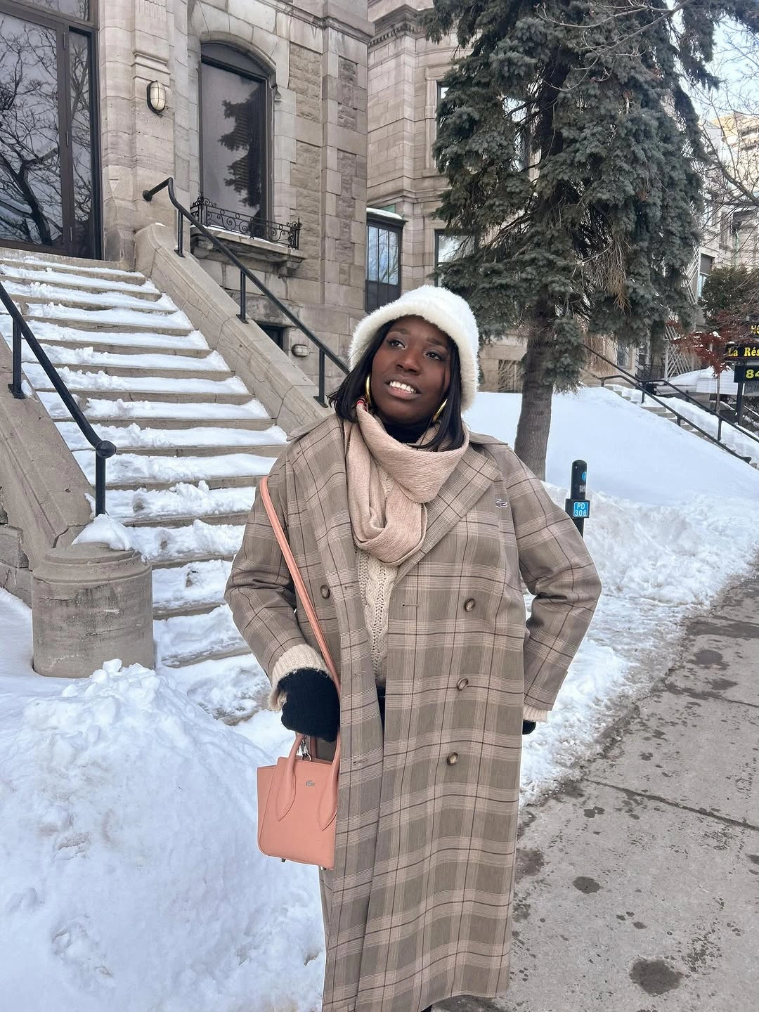 Beige plaid coat, pale scarf, white hat, black gloves, and pink handbag
