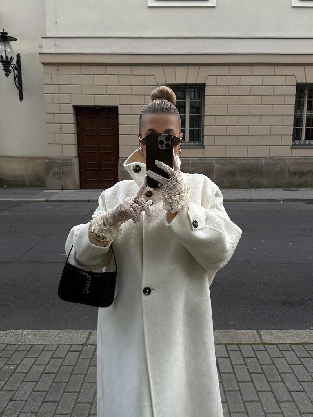 Long oversized white coat, pale accessories, and small black shoulder bag