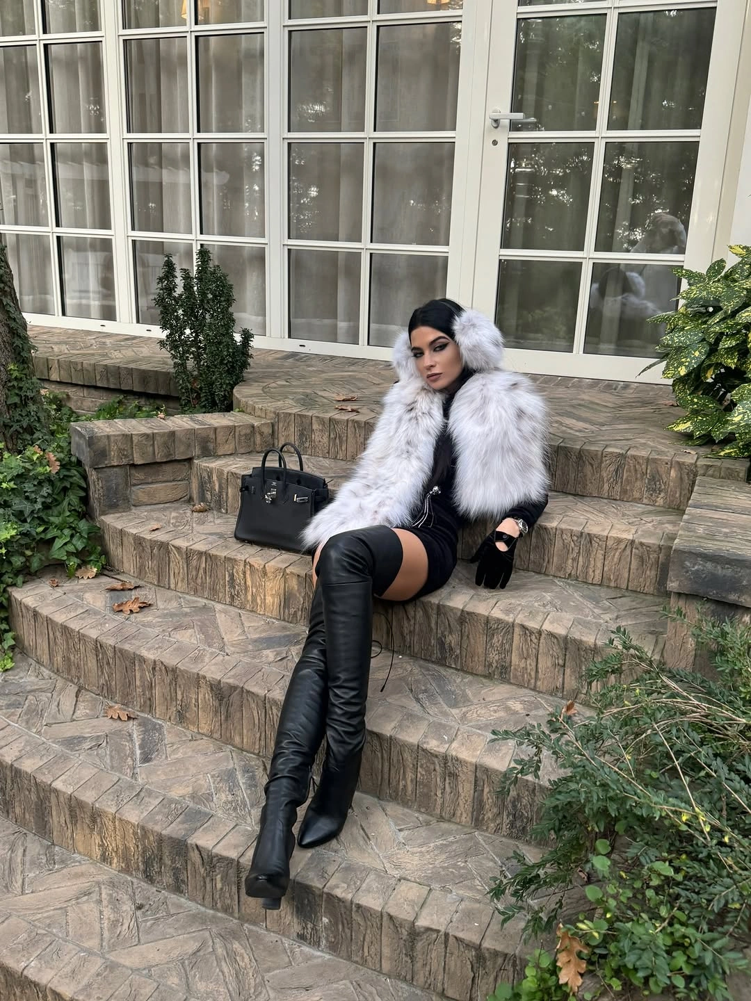 Pale shaggy outer layer, black short outfit, gloves, handbag, and tall boots
