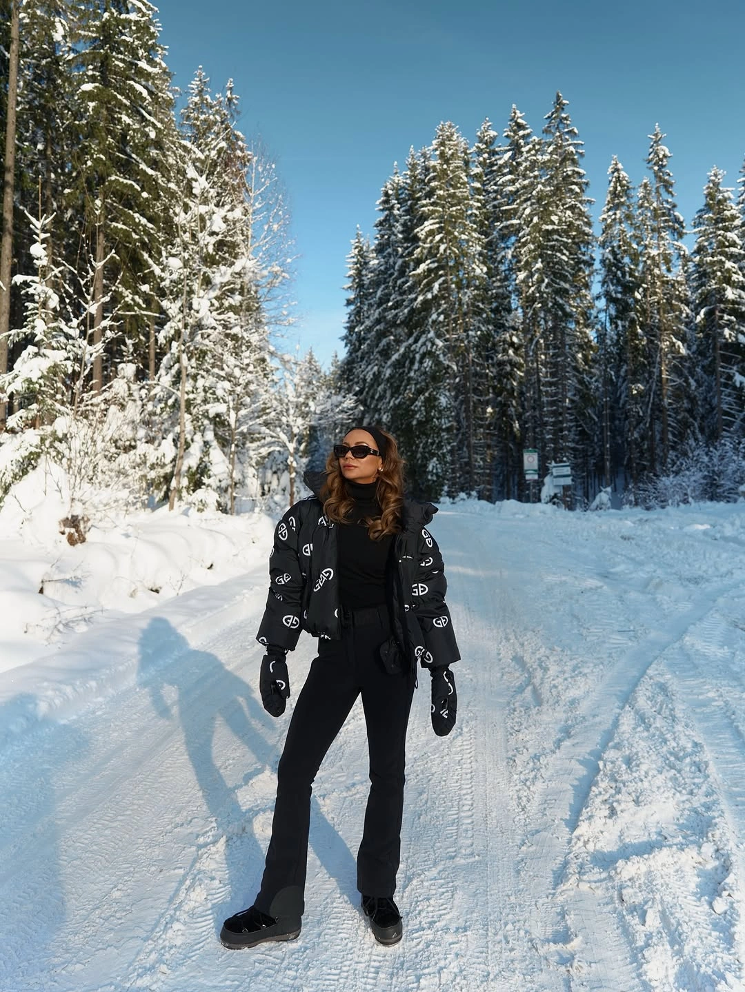 Black graphic jacket, fitted pants, gloves, sunglasses, and dark shoes on snowy road