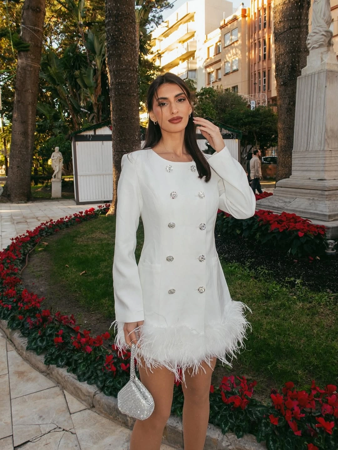 White long-sleeve mini dress with buttons, feather-like hem, and silver-tone handbag