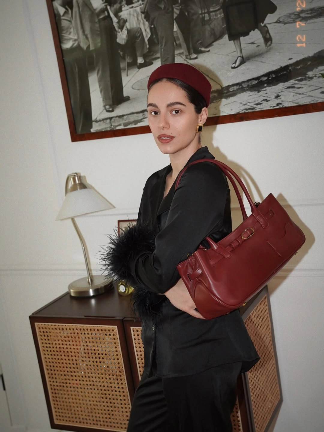 Black tailored suit, feather-like cuffs, deep red bag, red hat, and earrings