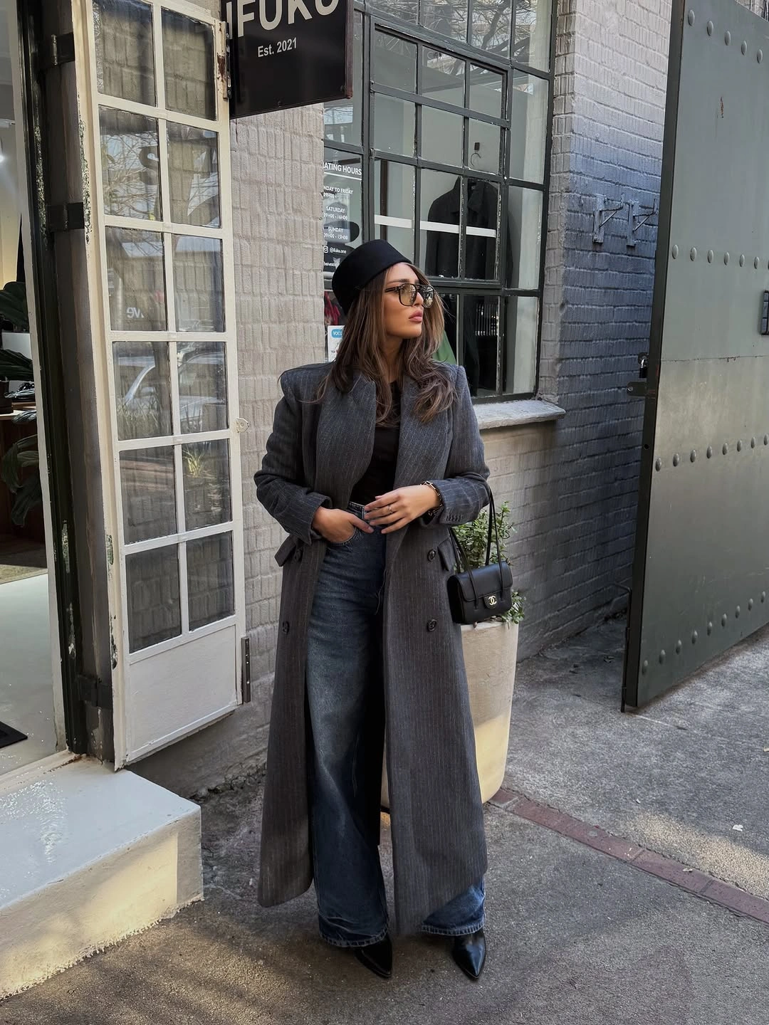 Long charcoal coat, gray top, wide jeans, black beanie, bag, and pointed shoes