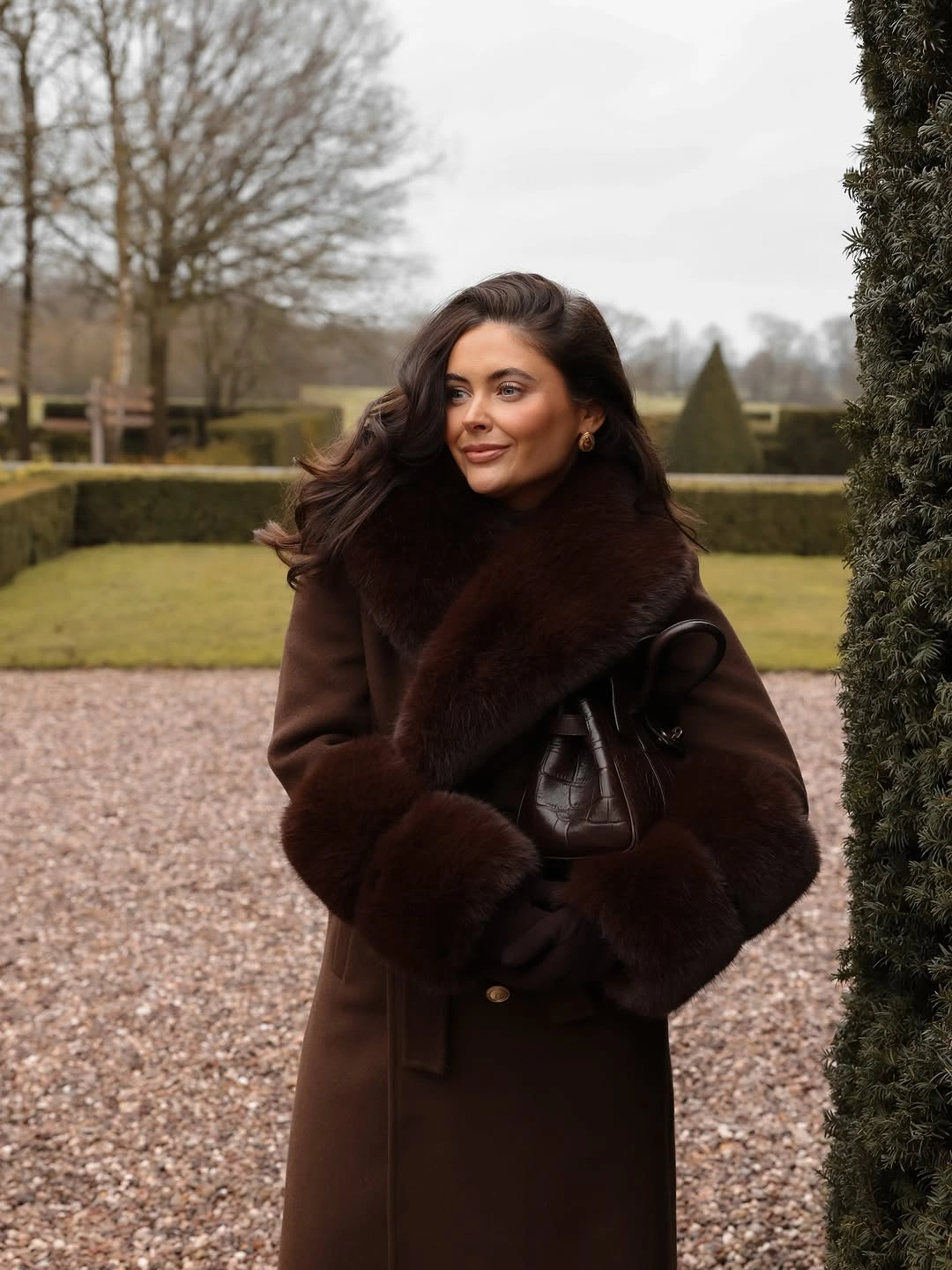 Long dark brown coat with shaggy collar and cuffs, plus black handbag