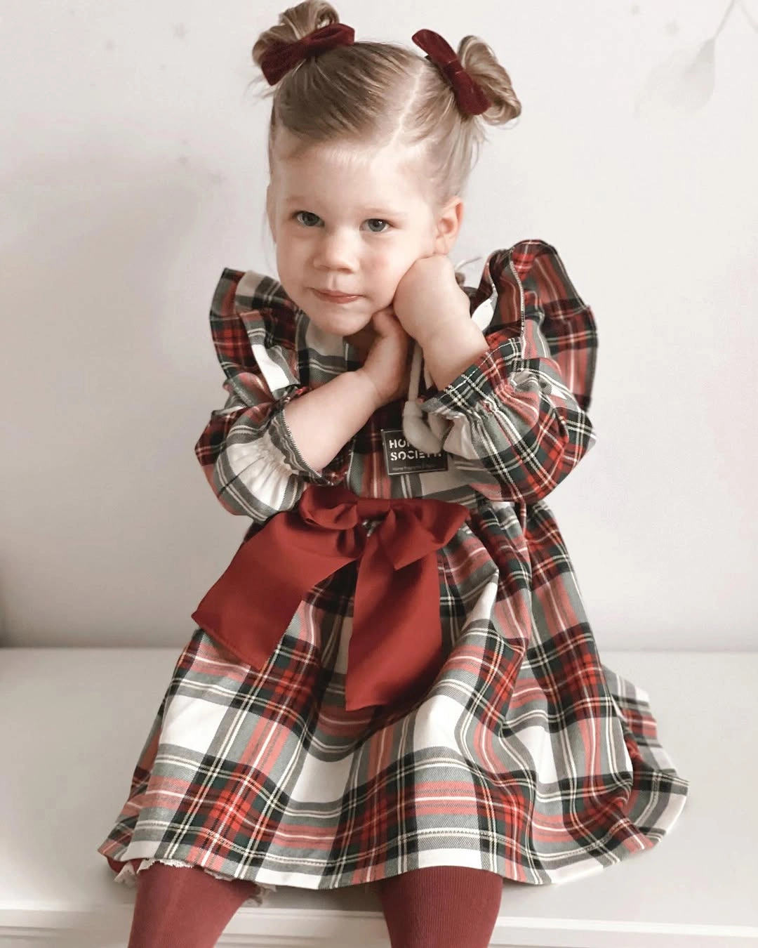 Child in plaid dress with shoulder ruffles and red waist bow