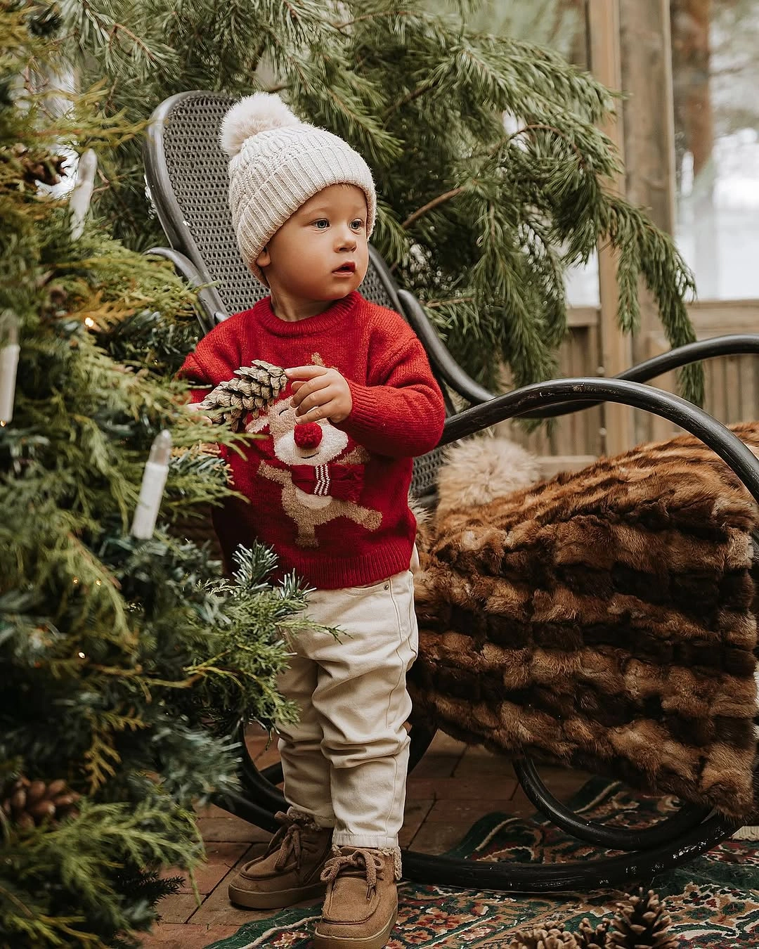 Child in red sweater cream pants and pom-pom hat