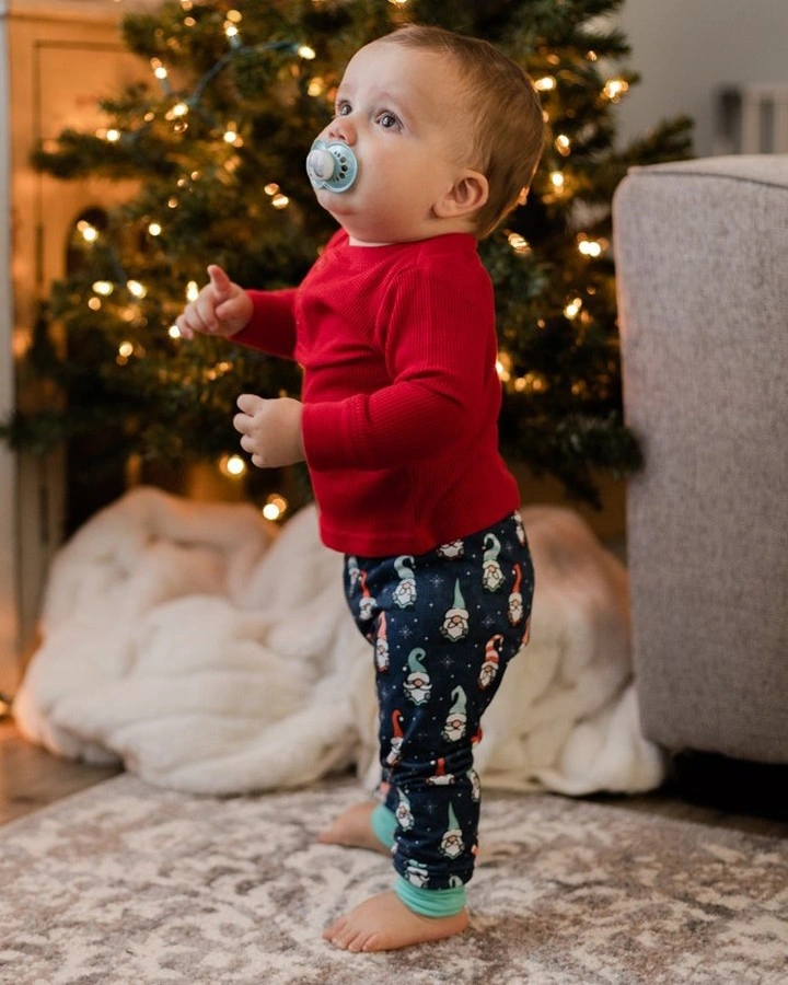 Child in red top and dark printed pants by Christmas tree