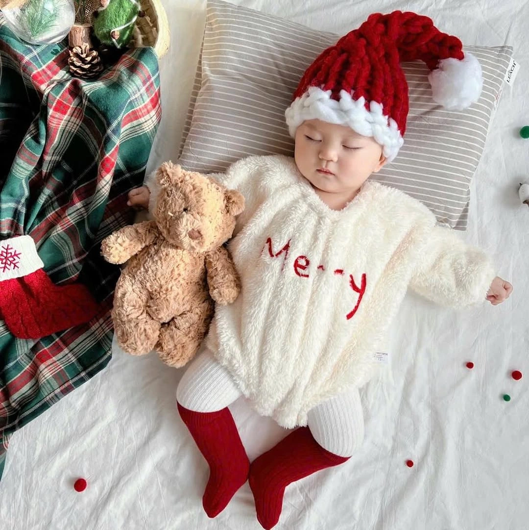 Child in white outfit with red socks and Santa-style hat