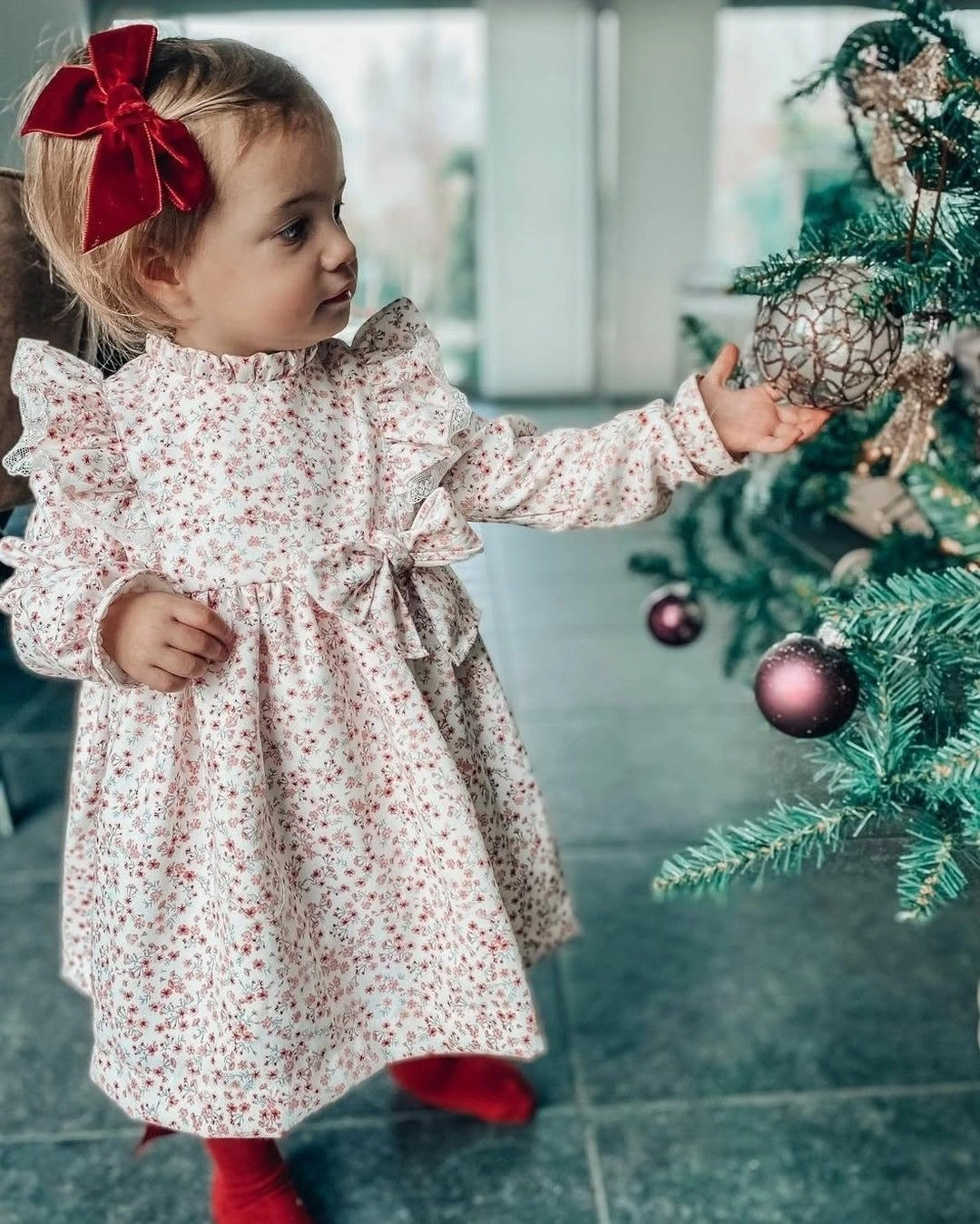 Child in pale floral dress with red bow and tights