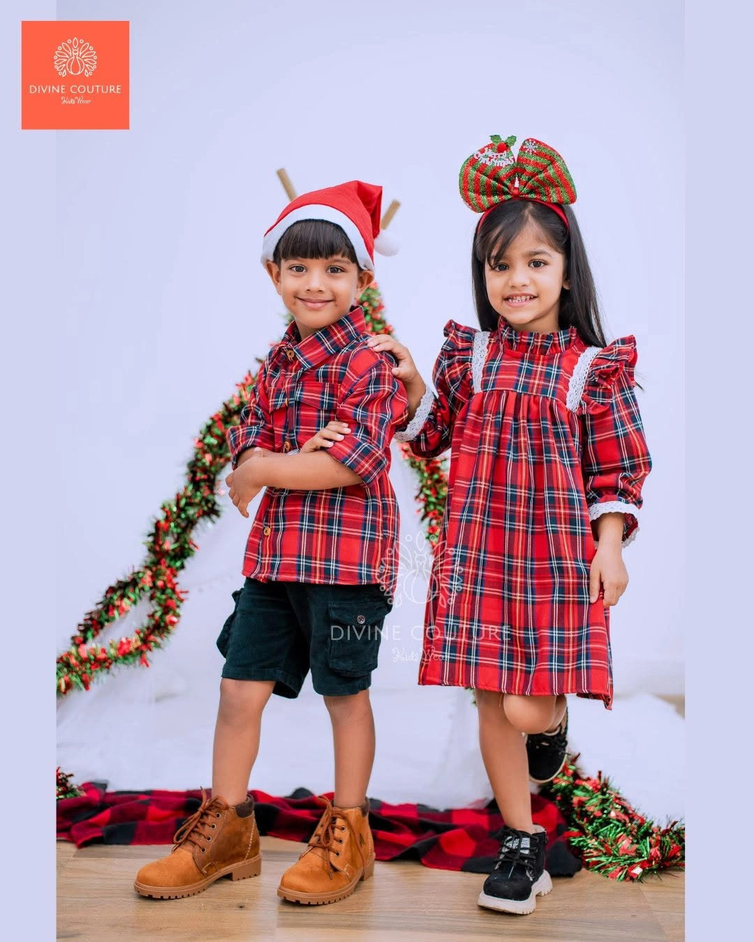 Two children wearing coordinated red plaid outfits and festive headwear