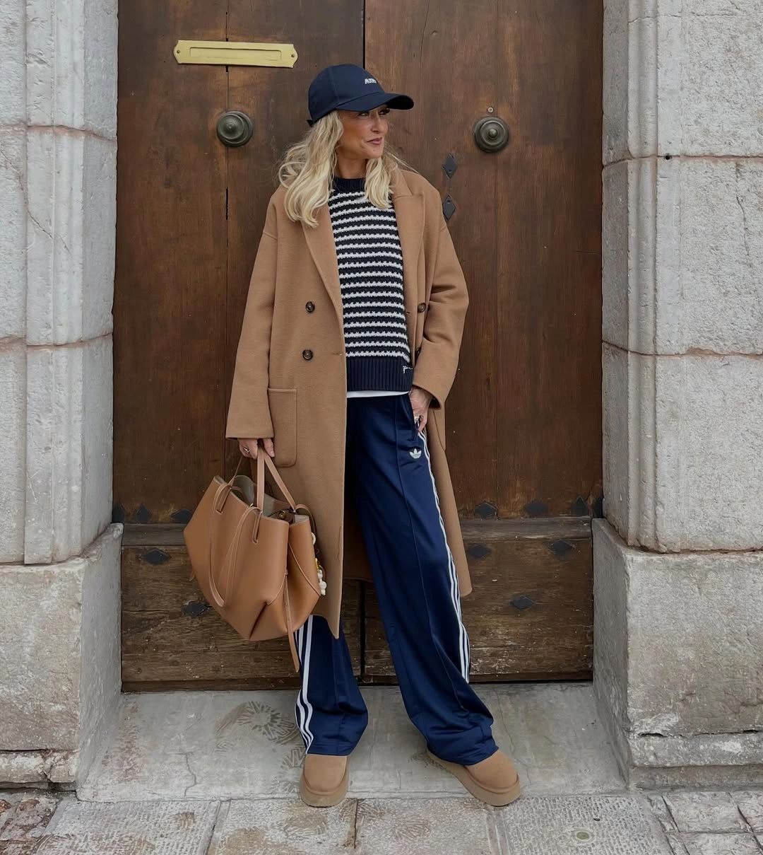 Camel blazer with striped sweater, navy side-striped pants, cap, tan bag, and boots