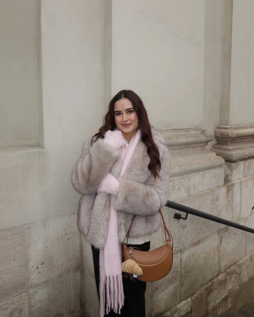 Pale textured jacket with soft pink scarf, black bottoms, and tan shoulder bag