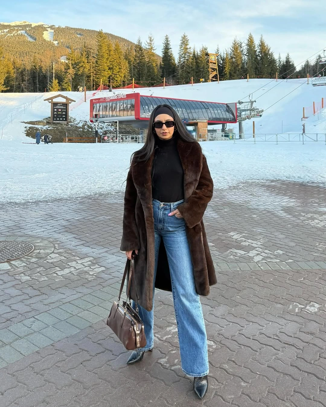 Long brown textured coat with black top, blue flared jeans, pointed shoes, and brown bag
