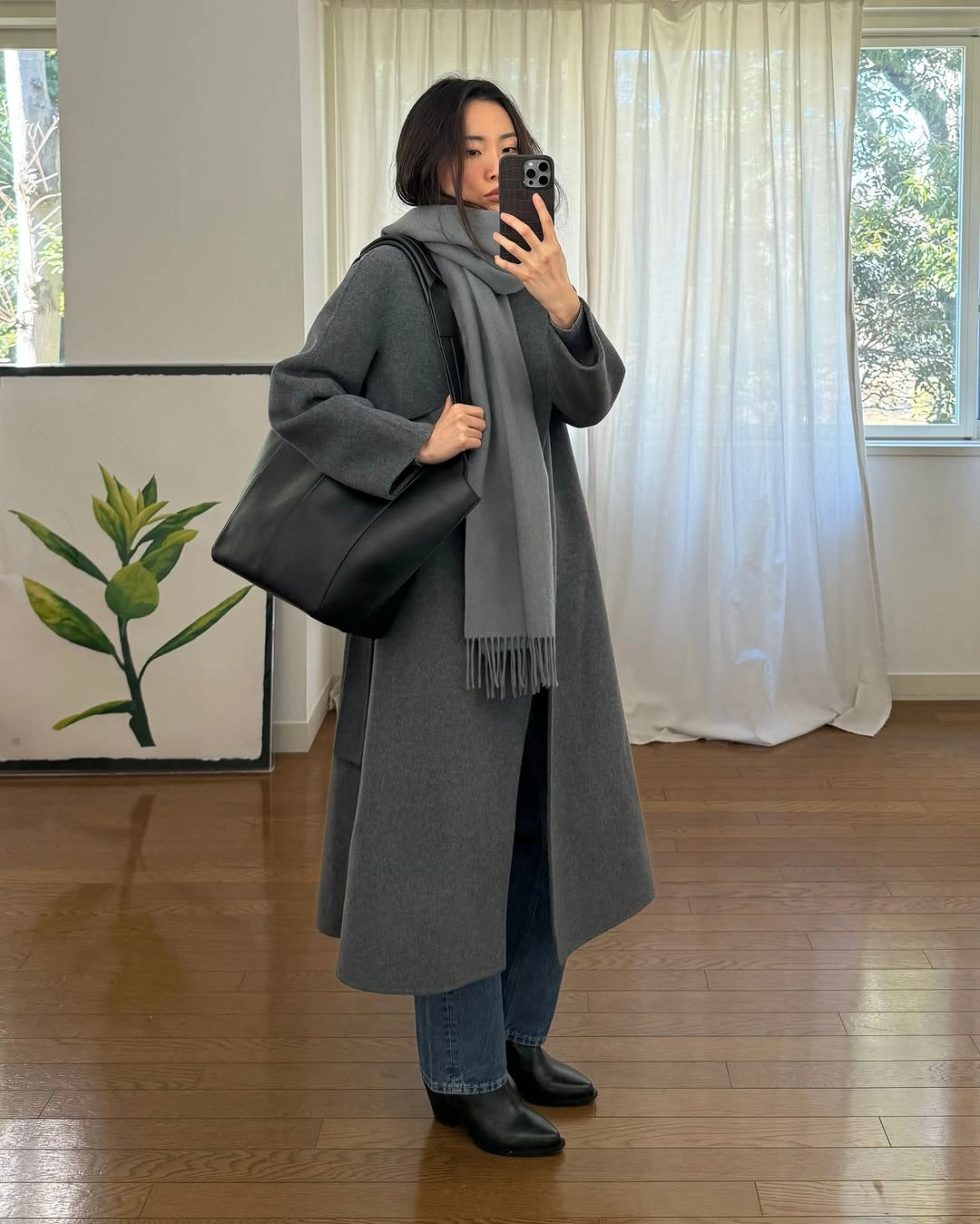 Long charcoal coat with dark jeans, black ankle boots, and oversized black shoulder bag