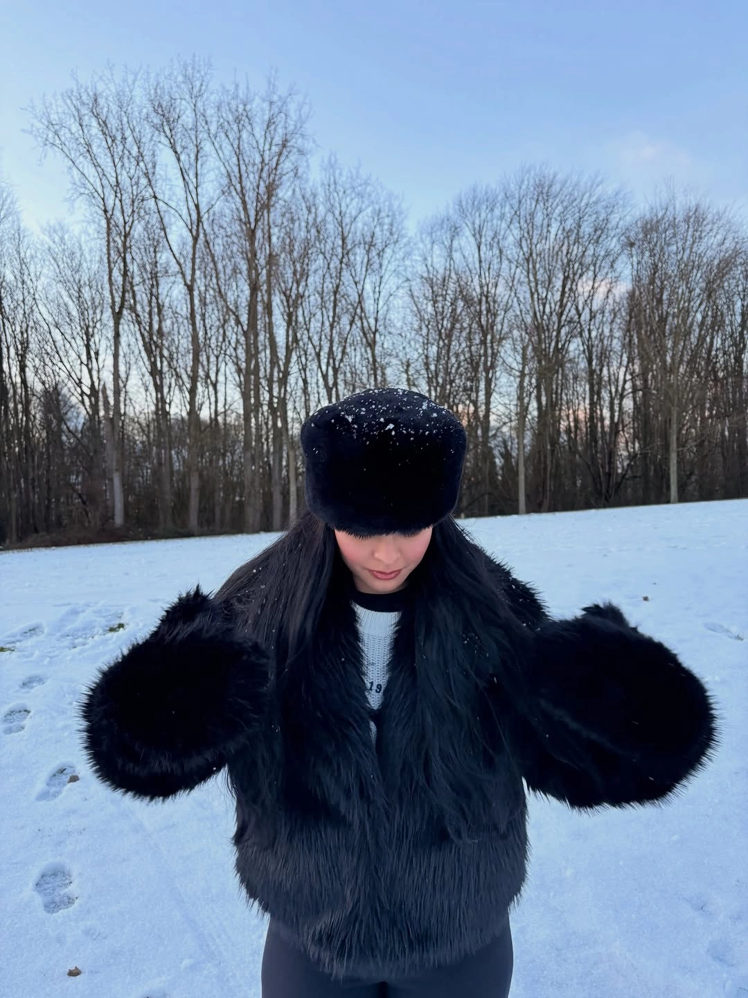 Black fuzzy jacket with dark textured hat and dark winter layers in snow