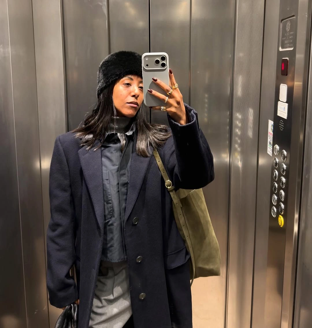 Dark tailored coat with black beanie, gray pants, and olive canvas tote
