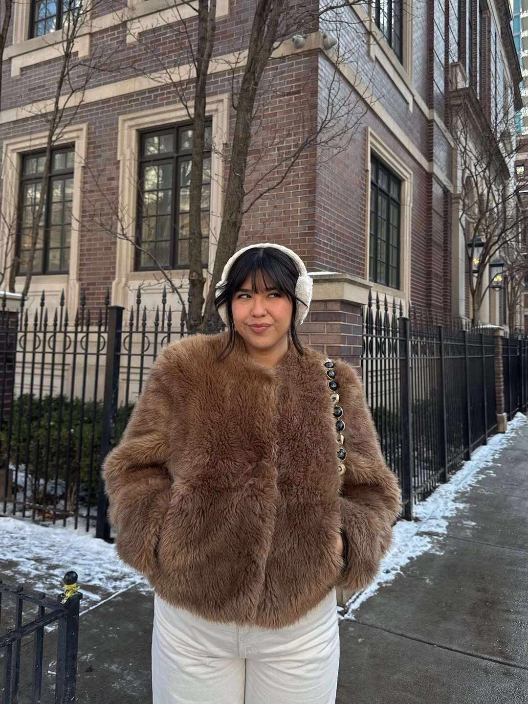 Warm brown textured sweater with white trousers, dark headwear, and small bag