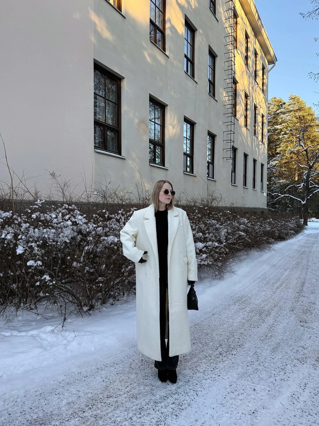 Long white textured coat over black outfit with small dark bag