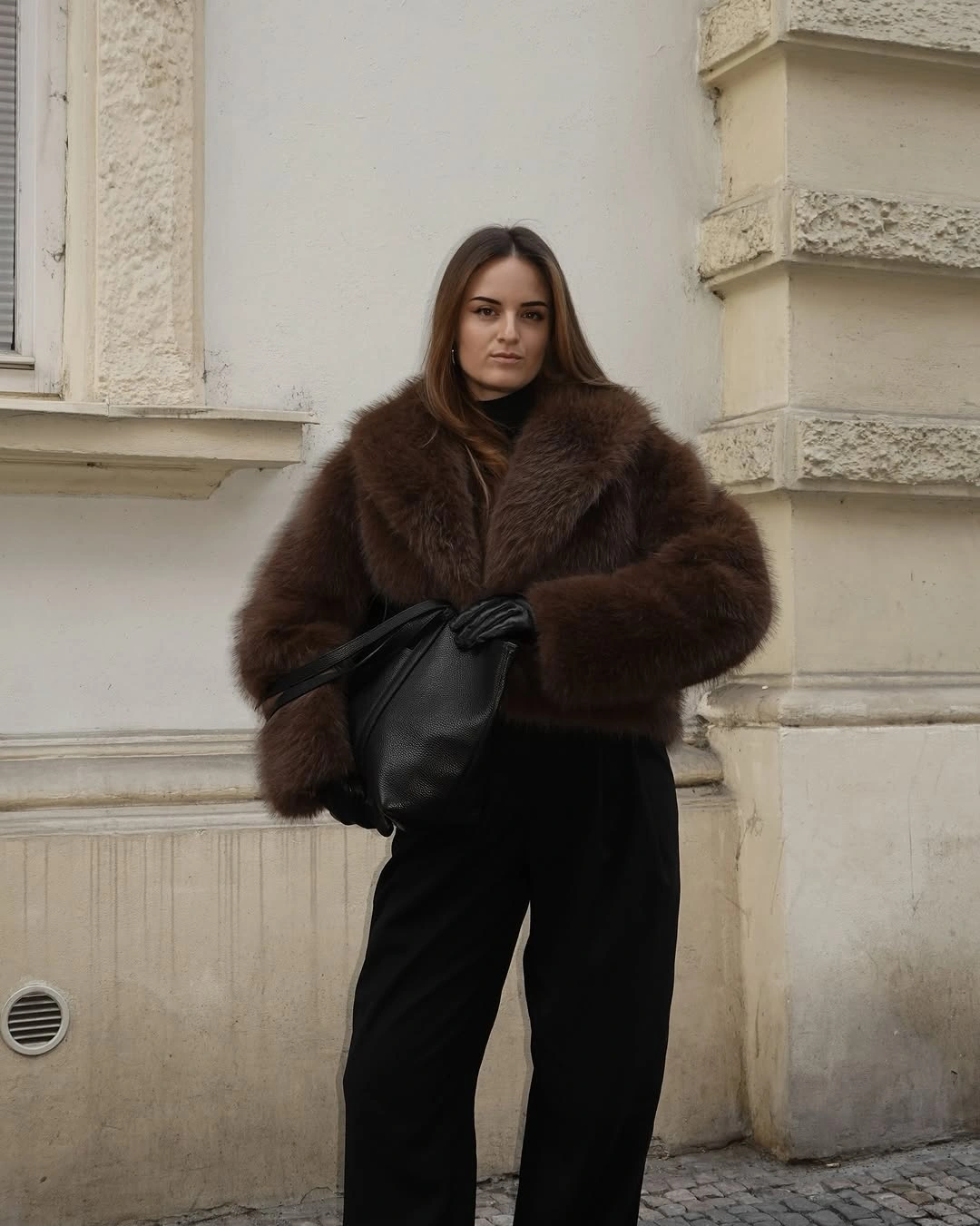 Short brown textured jacket with black trousers, gloves, and slouchy bag