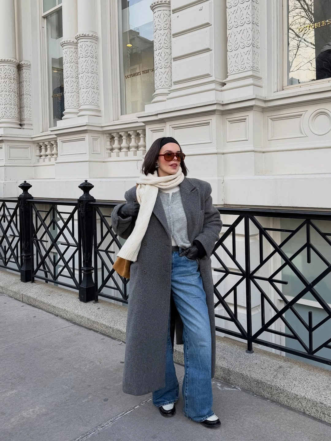 Long gray coat with cream scarf, cardigan, blue jeans, gloves, and bag