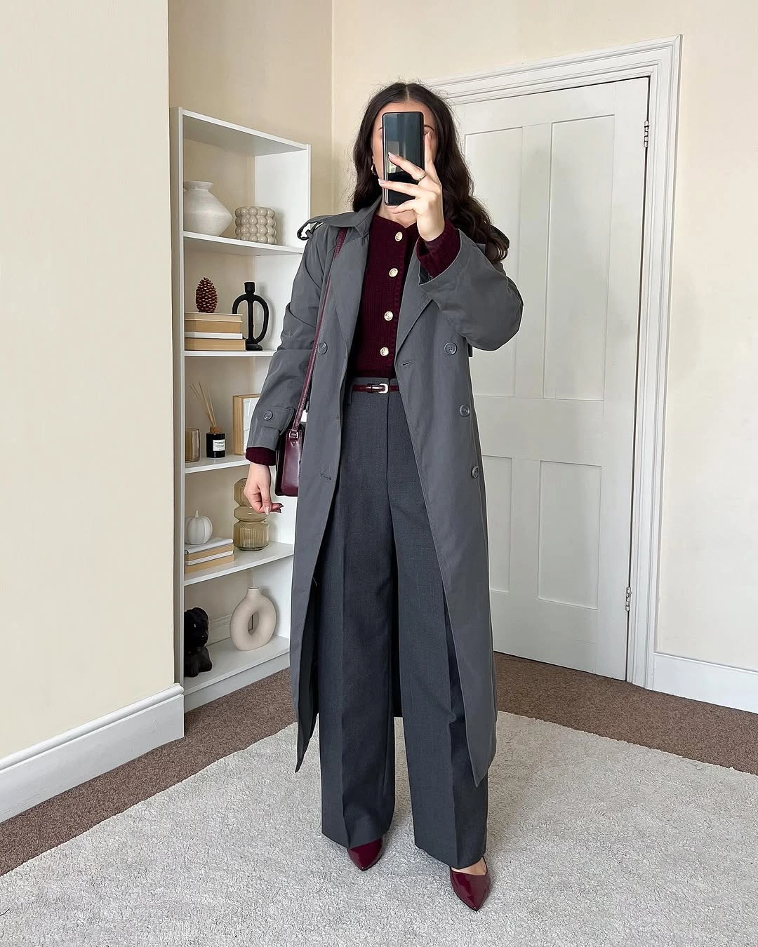 Gray coat and charcoal trousers with burgundy cardigan, belt, bag, and pointed shoes