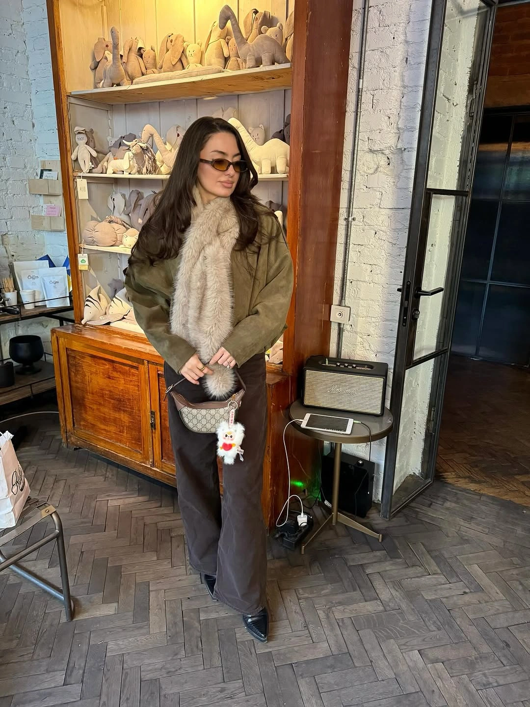 Olive-brown jacket with pale plush scarf, wide brown trousers, and patterned bag