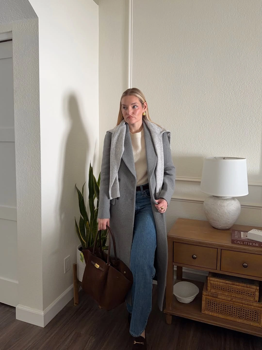 Gray coat with shoulder-draped knit, cream top, blue jeans, and brown tote